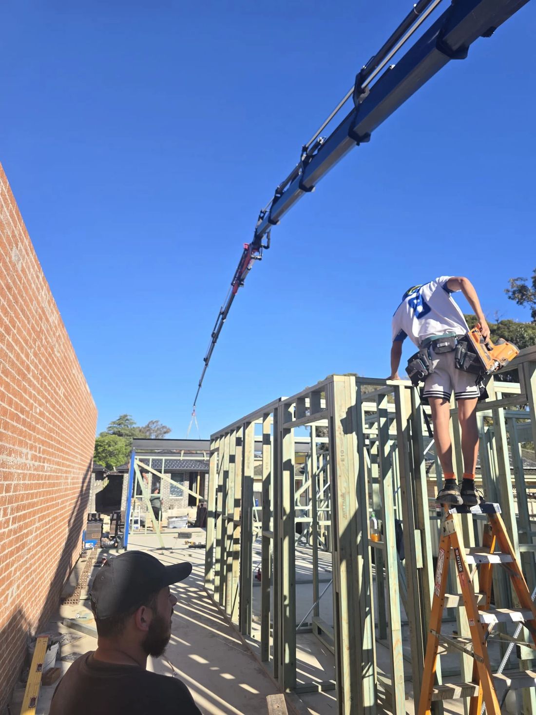 Knuckle boom crane lifting over wall frames