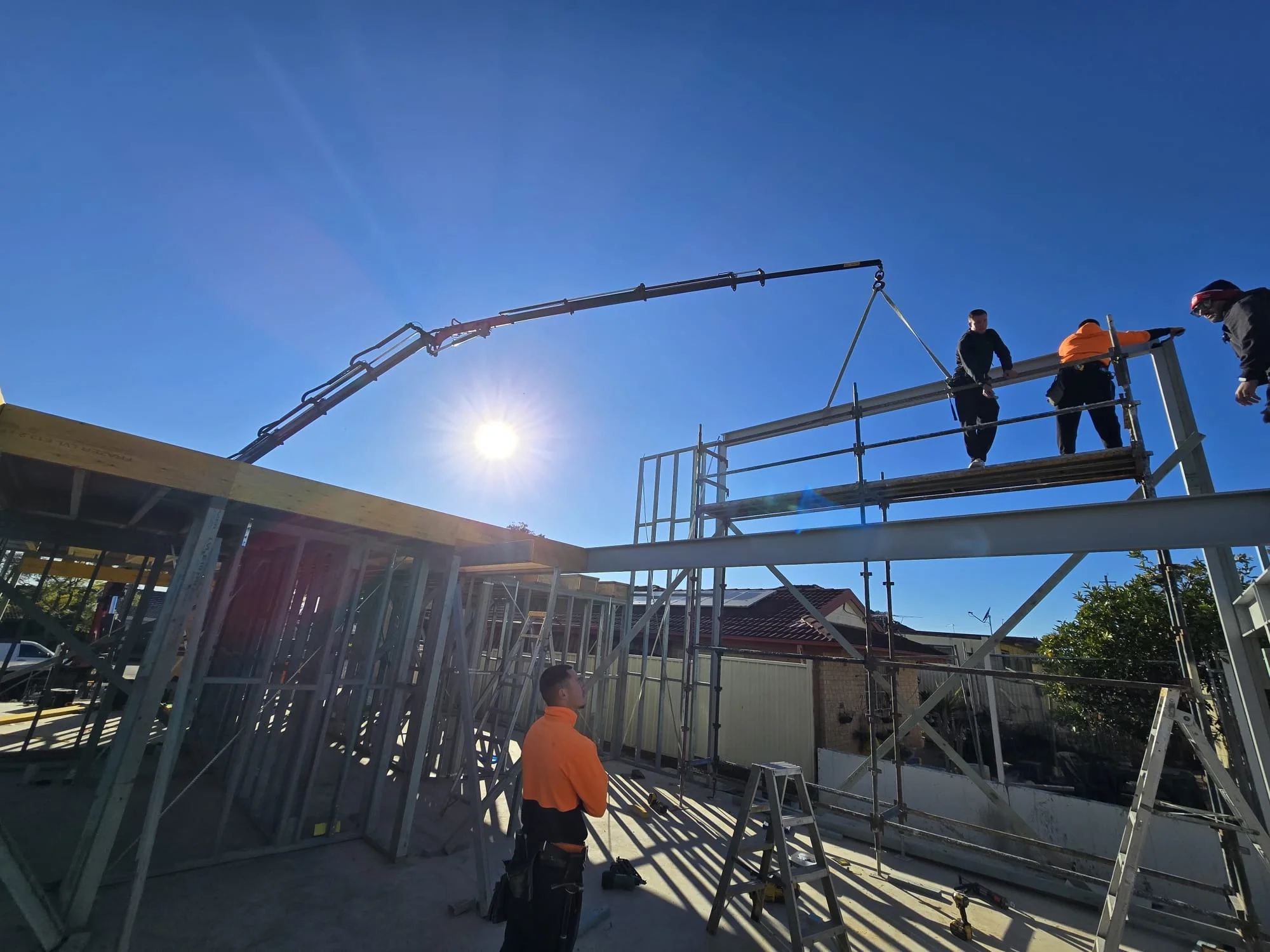 Crane lifting steel over a rooftop scaffold with workers guiding the load